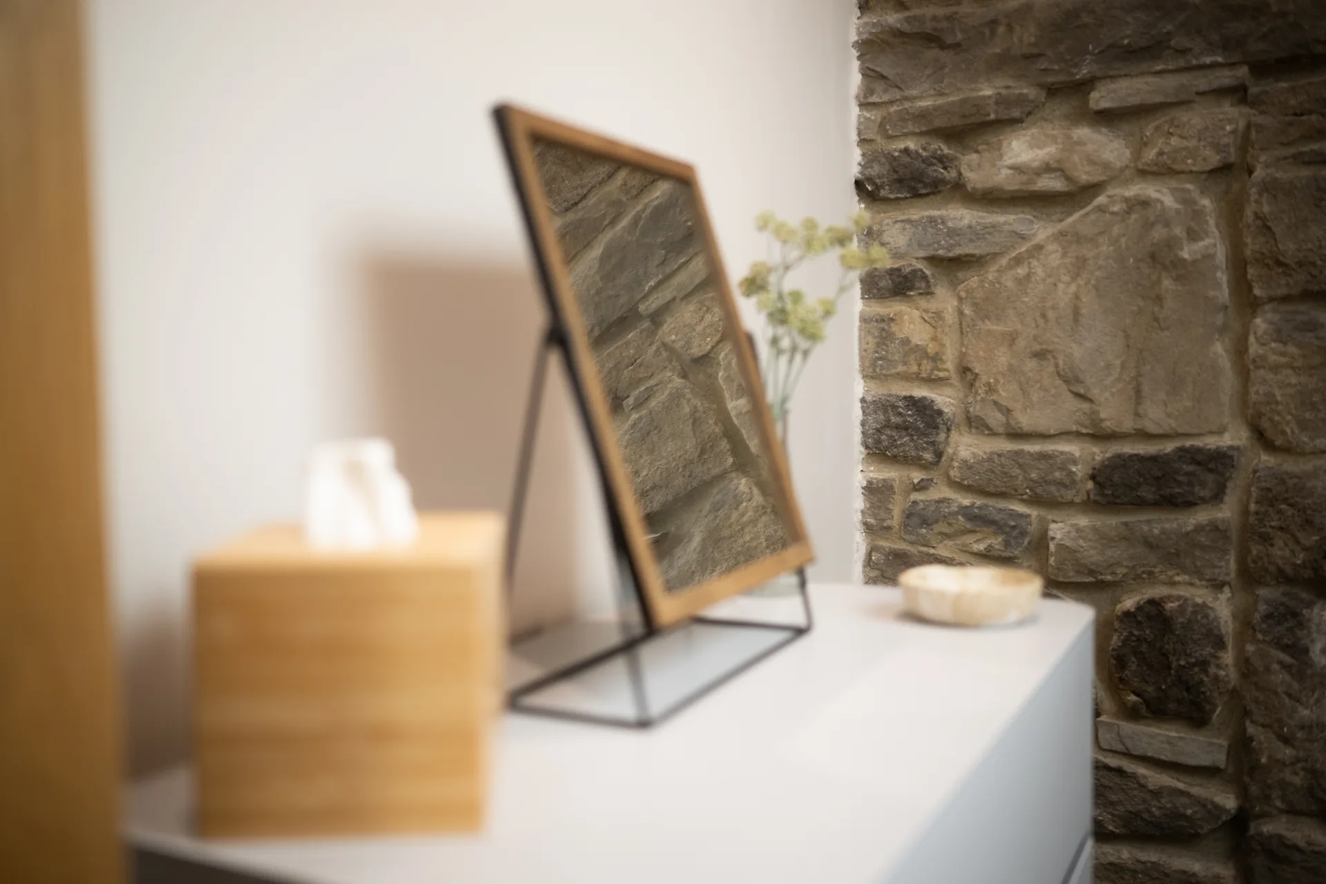 Tabletop mirror and tissue box beside an exposed stone wall