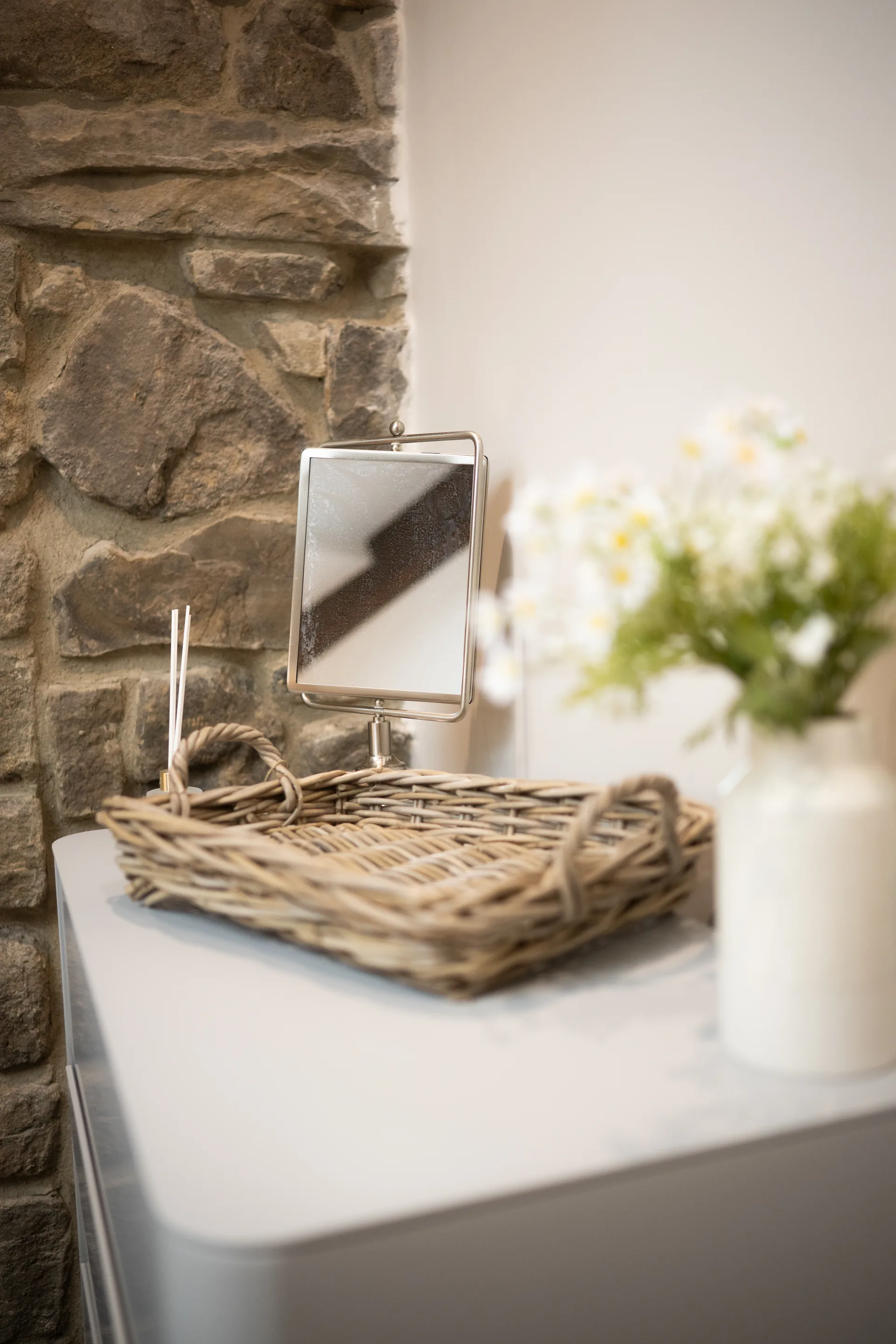 Wicker tray and tabletop mirror beside a vase of flowers